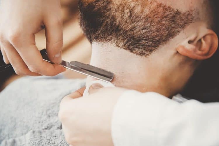 Barber helps shave a neck beard clean with a straight razor.