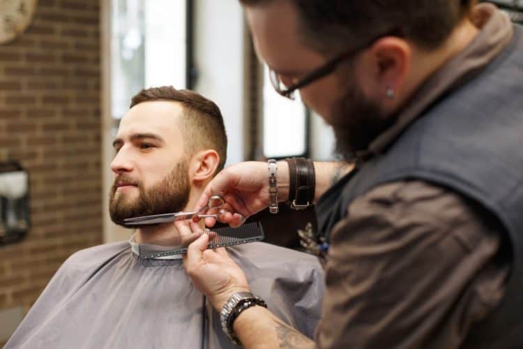 Barber styling beard with scissors to client at barbershop