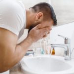 Man washes his face in bathroom, morning hygiene